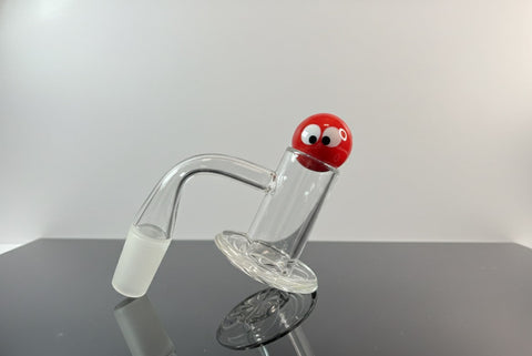 Clear quartz blender banger with a red marble with eyes on a reflective surface and a white neutral backround 